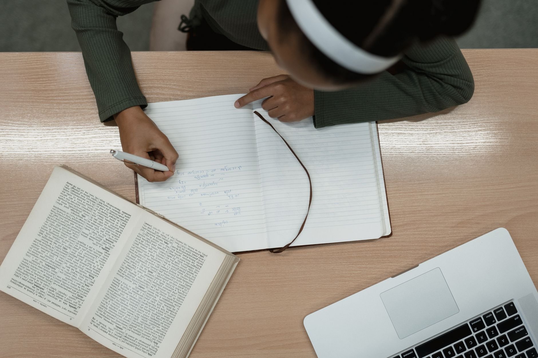 Top view of a person studying with an open book and laptop, writing notes in a notebook.